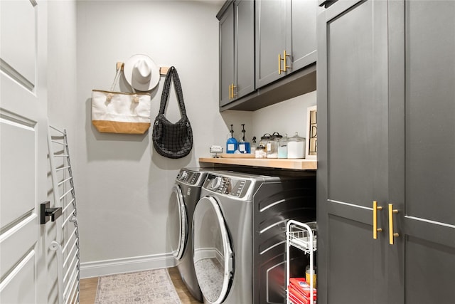 washroom featuring wood finished floors, washing machine and clothes dryer, cabinet space, and baseboards