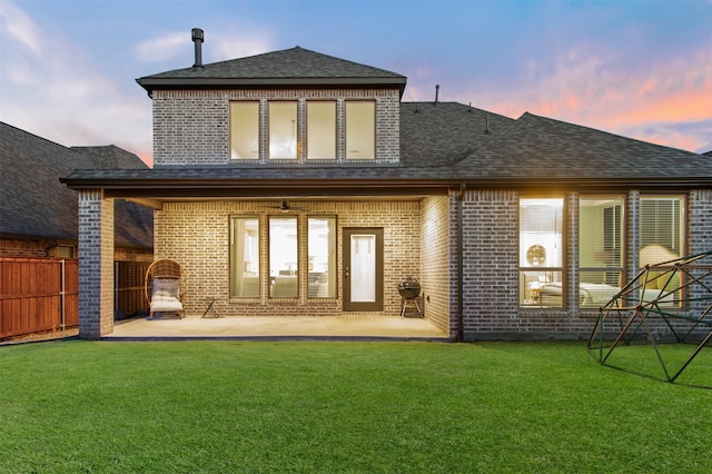 back of property at dusk with fence, a patio area, and brick siding