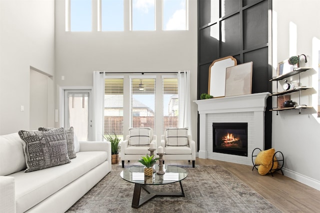 living room featuring a fireplace, wood finished floors, baseboards, and a high ceiling