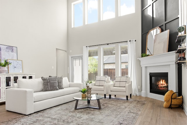 living area featuring wood finished floors, a healthy amount of sunlight, a high ceiling, and a brick fireplace