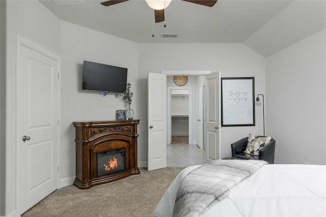 bedroom featuring a glass covered fireplace, ceiling fan, visible vents, vaulted ceiling, and light carpet