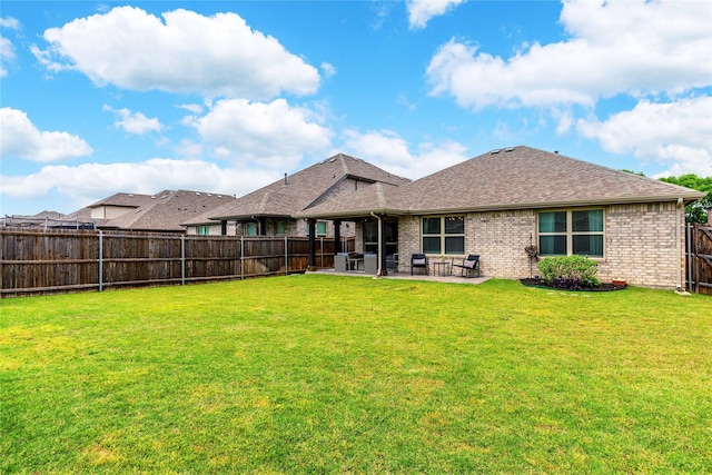 back of property featuring a lawn, brick siding, a patio area, roof with shingles, and a fenced backyard
