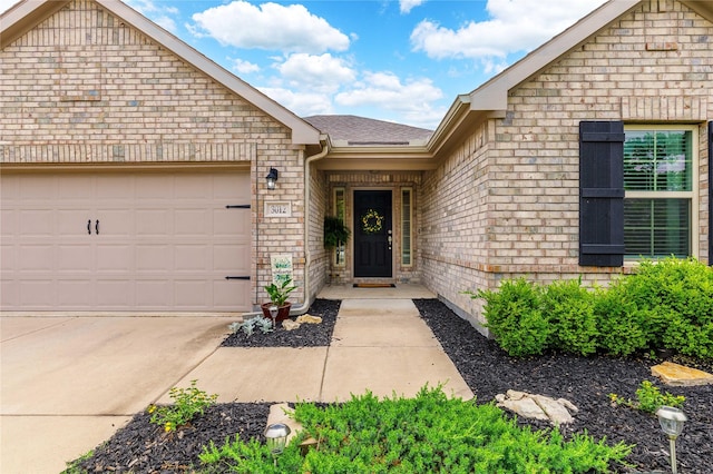 doorway to property featuring driveway, a shingled roof, brick siding, and an attached garage