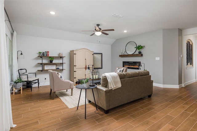 living area with visible vents, ceiling fan, light wood-style flooring, baseboards, and a glass covered fireplace