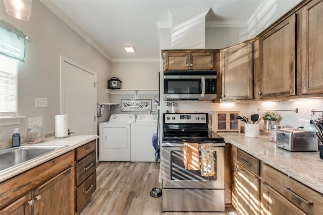 kitchen featuring light wood finished floors, stainless steel appliances, brown cabinetry, crown molding, and washer and dryer