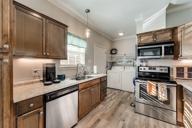 kitchen with a sink, stainless steel appliances, washer and dryer, light wood-type flooring, and ornamental molding