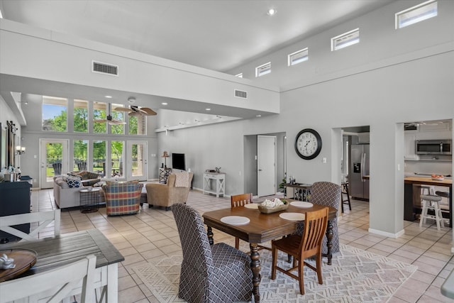 dining room with light tile patterned flooring, visible vents, ceiling fan, and a towering ceiling