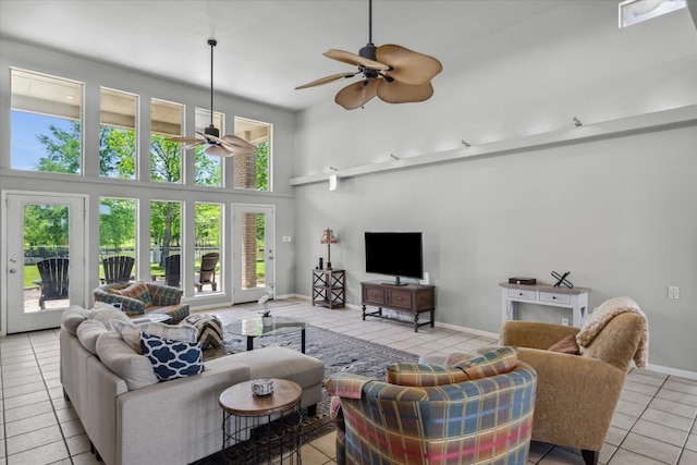 living area featuring tile patterned floors, a ceiling fan, baseboards, and a high ceiling