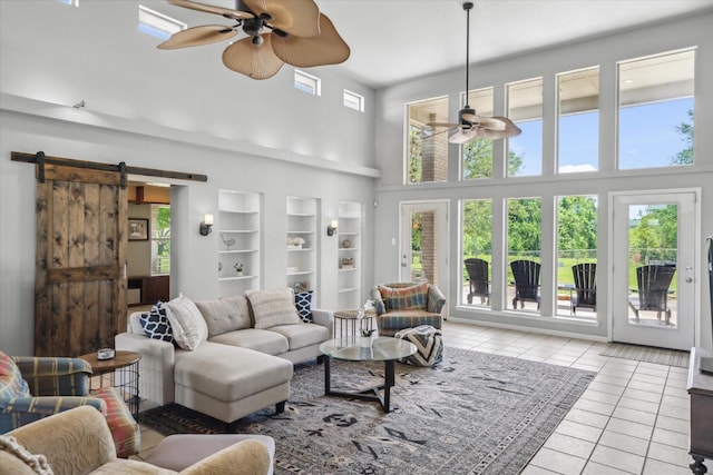 living area featuring light tile patterned flooring, ceiling fan, a high ceiling, and a barn door