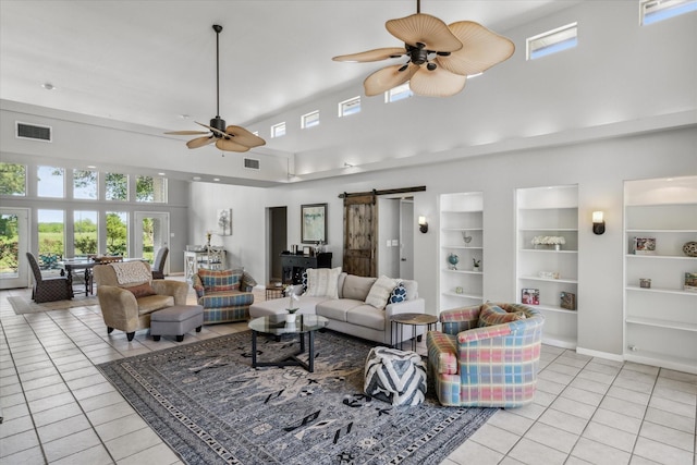 living area featuring light tile patterned floors, a barn door, visible vents, a towering ceiling, and a ceiling fan