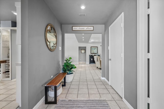 hallway with baseboards, visible vents, and light tile patterned floors