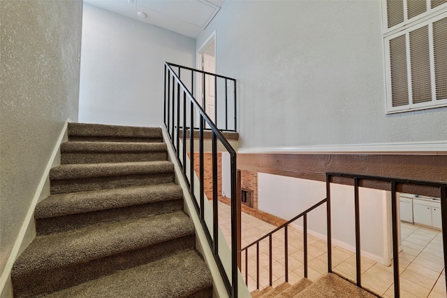 stairs featuring a textured wall, tile patterned floors, and attic access