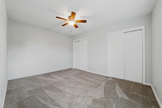 unfurnished bedroom featuring two closets, brick wall, carpet floors, and ceiling fan