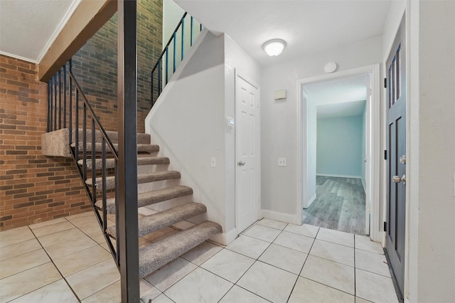 stairway featuring baseboards, brick wall, and tile patterned floors