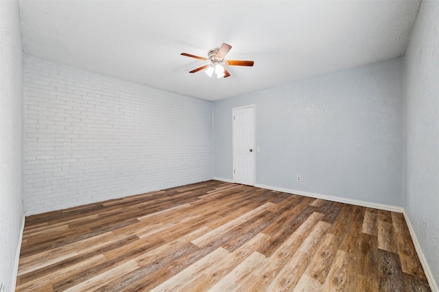 unfurnished room featuring baseboards, ceiling fan, wood finished floors, and brick wall