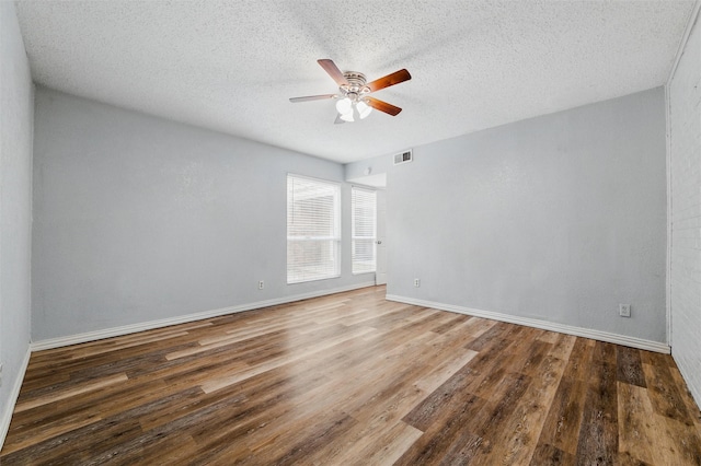 empty room with ceiling fan, a textured ceiling, baseboards, wood finished floors, and visible vents