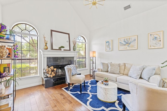living area with a tiled fireplace, visible vents, wood finished floors, baseboards, and high vaulted ceiling