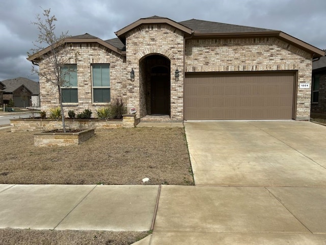 french country home with brick siding, a shingled roof, concrete driveway, and an attached garage