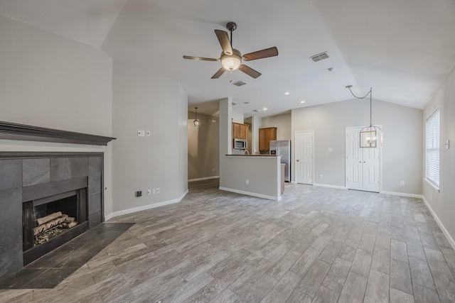unfurnished living room featuring visible vents, ceiling fan with notable chandelier, a fireplace, light wood-type flooring, and lofted ceiling