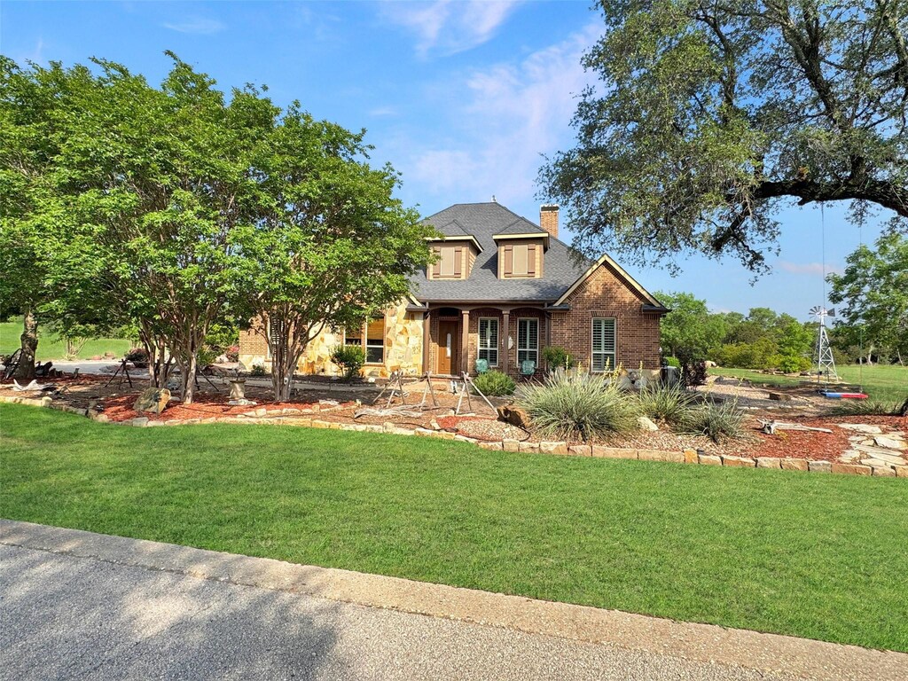craftsman house featuring a chimney, brick siding, a shingled roof, and a front lawn