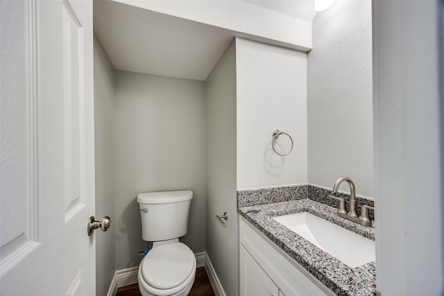 bathroom with toilet, vanity, wood finished floors, and baseboards