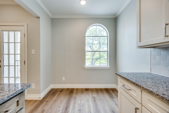 unfurnished dining area featuring baseboards, light wood-type flooring, and ornamental molding
