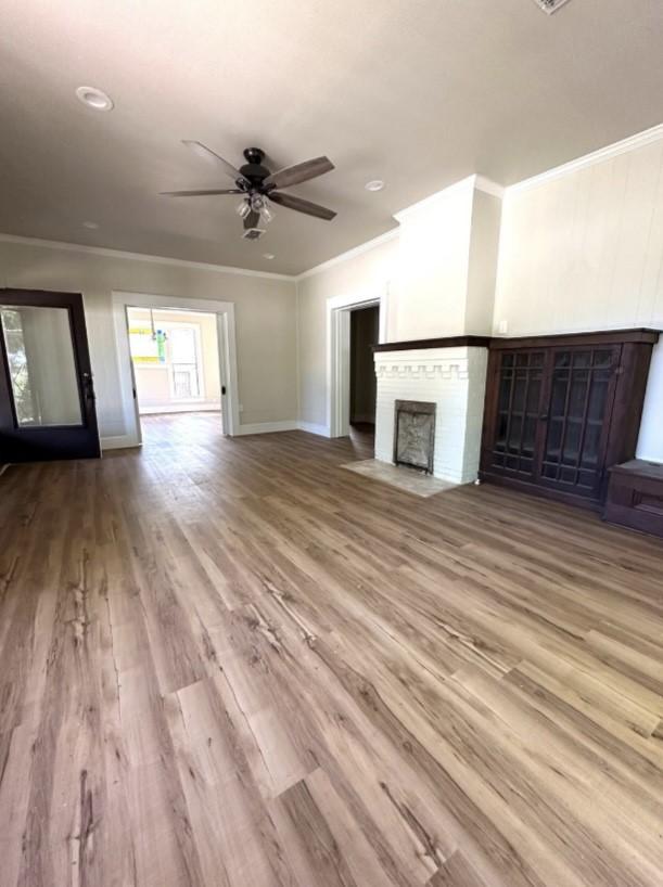 unfurnished living room featuring a fireplace with flush hearth, wood finished floors, crown molding, and a ceiling fan