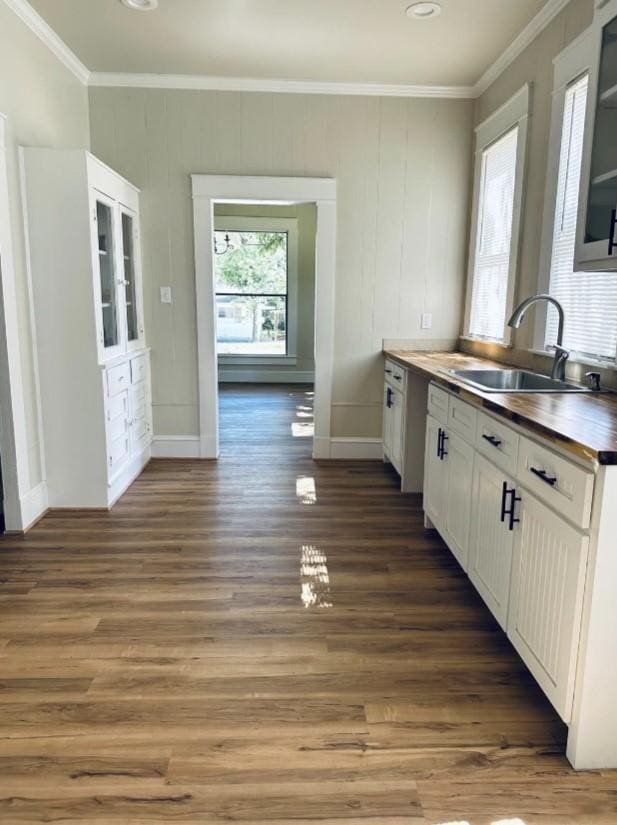kitchen with crown molding, white cabinets, a sink, butcher block counters, and dark wood finished floors