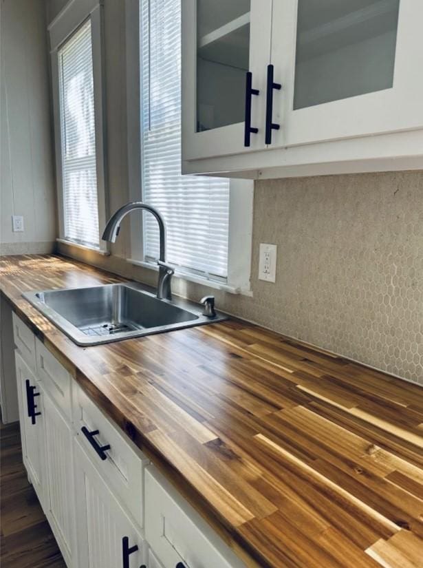 kitchen with wooden counters, a sink, white cabinets, and dark wood-type flooring