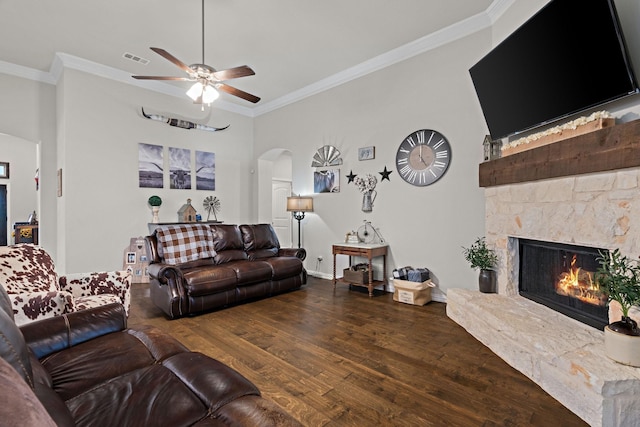 living room with ceiling fan, crown molding, a stone fireplace, arched walkways, and wood finished floors