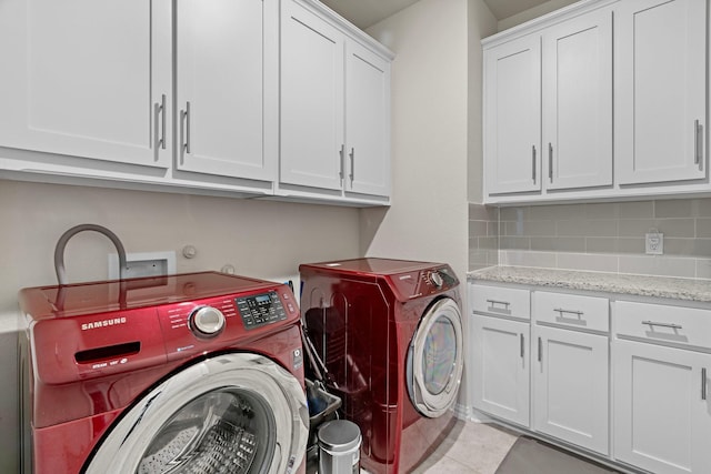 laundry area featuring light tile patterned floors, washing machine and clothes dryer, and cabinet space