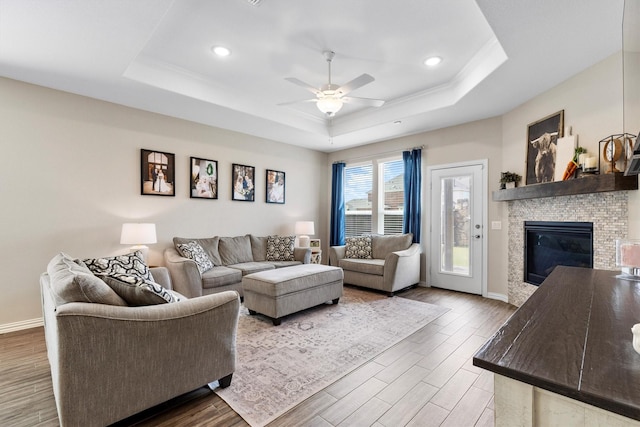 living room featuring wood finished floors, a raised ceiling, ceiling fan, and a stone fireplace
