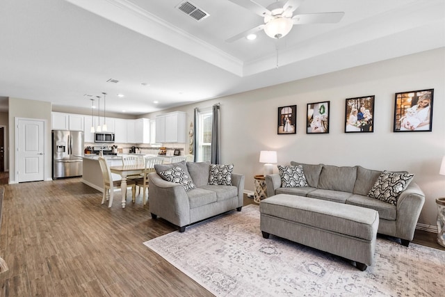 living area featuring recessed lighting, light wood-type flooring, ceiling fan, visible vents, and a tray ceiling