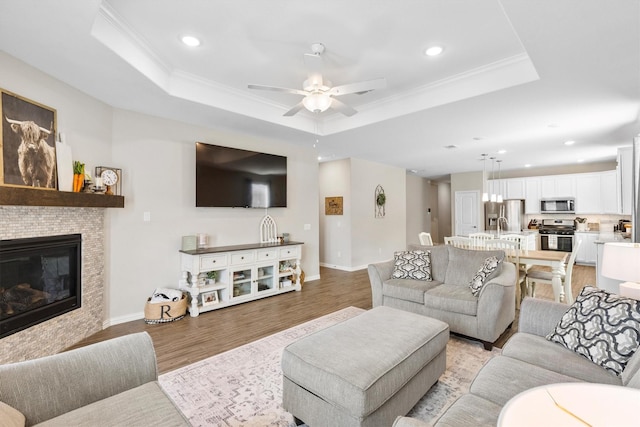 living area with a raised ceiling, light wood-type flooring, a ceiling fan, and recessed lighting