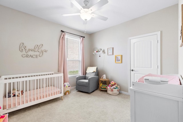 bedroom with baseboards, a nursery area, ceiling fan, and carpet flooring