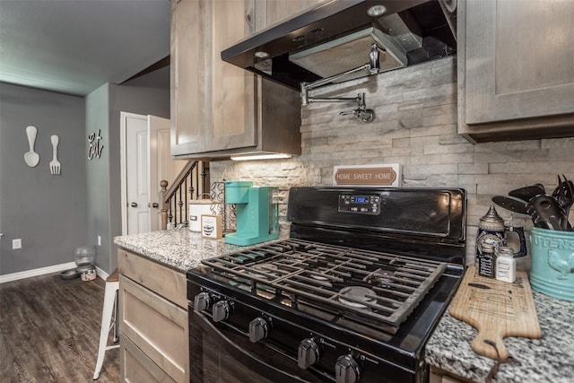 kitchen with wood finished floors, exhaust hood, light stone counters, baseboards, and black gas range