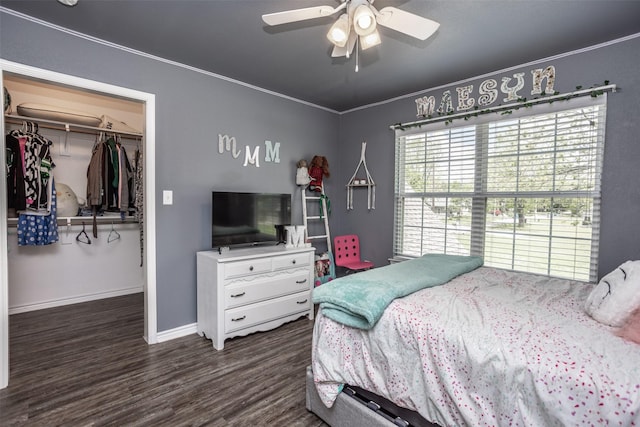 bedroom with wood finished floors, a closet, a walk in closet, baseboards, and crown molding