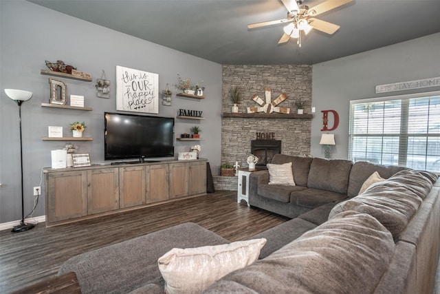 living room featuring dark wood finished floors, baseboards, a ceiling fan, and a stone fireplace