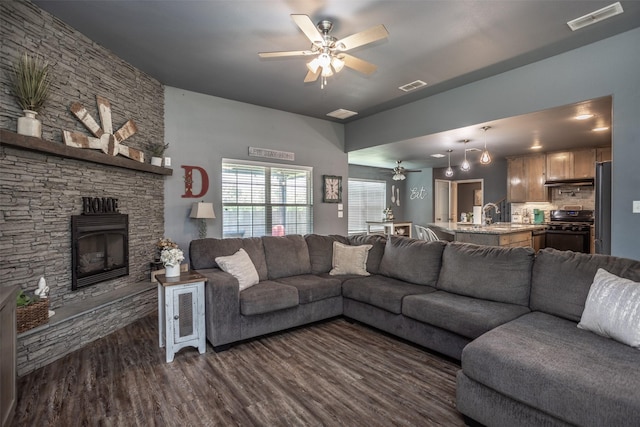 living room with a fireplace, dark wood-type flooring, visible vents, and a ceiling fan