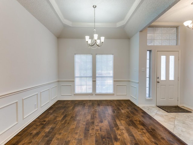 foyer entrance with a decorative wall, a raised ceiling, hardwood / wood-style floors, and a notable chandelier