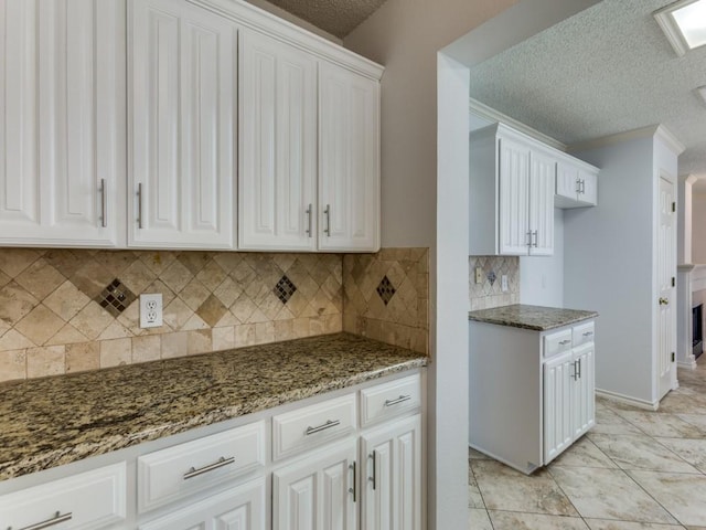 kitchen with dark stone countertops, a textured ceiling, white cabinetry, and decorative backsplash
