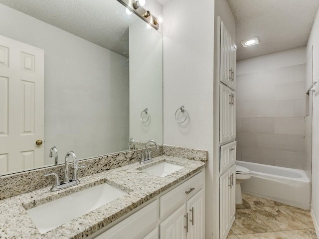 full bathroom with toilet, double vanity, a sink, and a textured ceiling