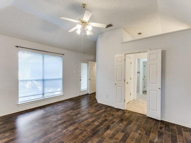 empty room with a textured ceiling, visible vents, vaulted ceiling, wood finished floors, and a ceiling fan