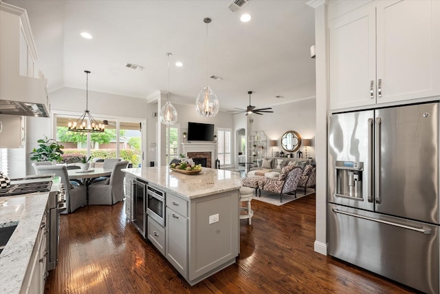 kitchen featuring visible vents, open floor plan, a fireplace, high quality appliances, and ceiling fan with notable chandelier