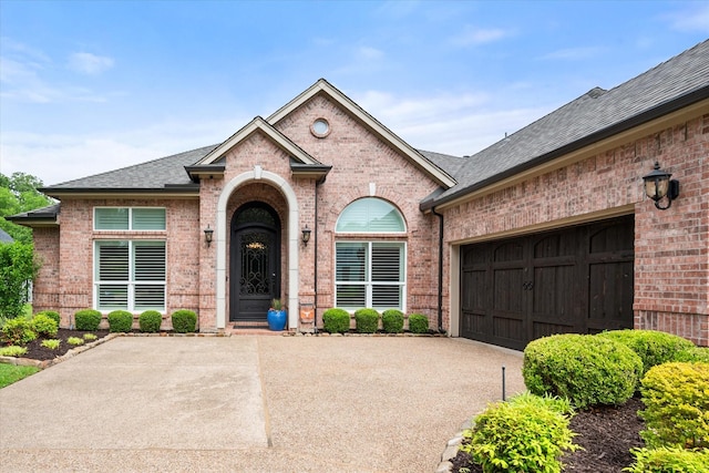 view of front of property featuring roof with shingles, an attached garage, driveway, and brick siding