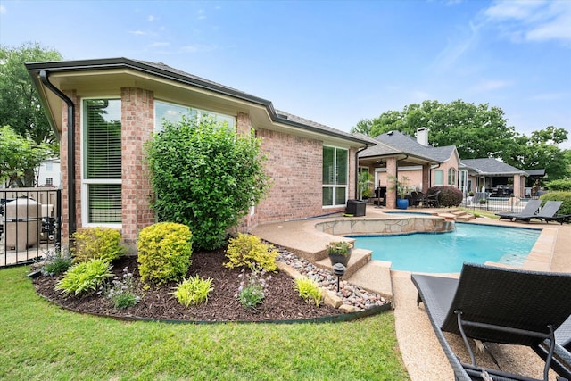 back of property featuring a patio area, an outdoor pool, an in ground hot tub, brick siding, and fence
