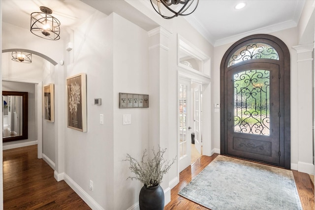 foyer entrance featuring an inviting chandelier, wood finished floors, crown molding, and arched walkways