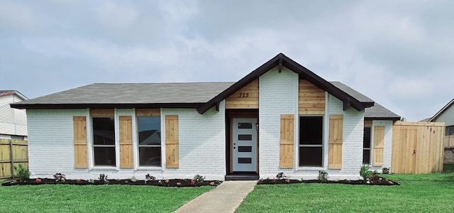 view of front of property with fence, roof with shingles, a front yard, and brick siding