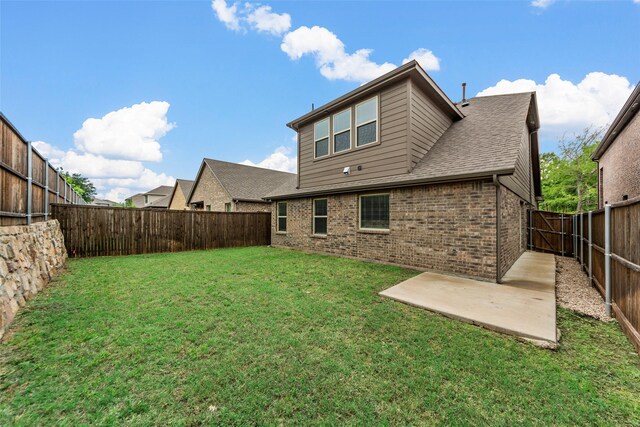 rear view of property with a lawn, a patio area, brick siding, a fenced backyard, and a shingled roof