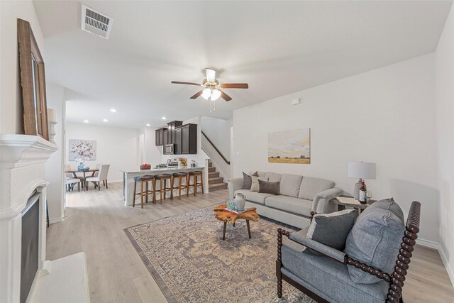 living room featuring stairs, ceiling fan, visible vents, and light wood finished floors